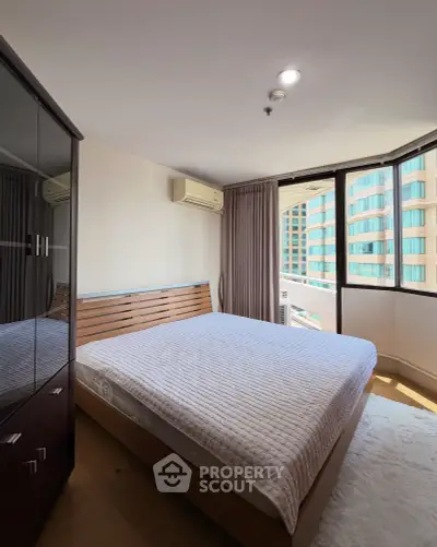 Spacious bedroom with large windows and modern furnishings in a high-rise apartment.
