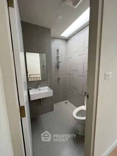 Modern bathroom with sleek gray tiles and skylight, featuring a wall-mounted sink and shower area.