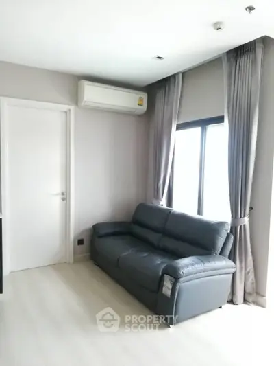 Modern living room with sleek black leather sofa and large window, featuring elegant curtains and air conditioning.