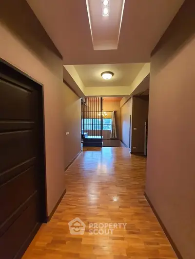 Spacious hallway with wooden flooring and modern lighting leading to a cozy living area.