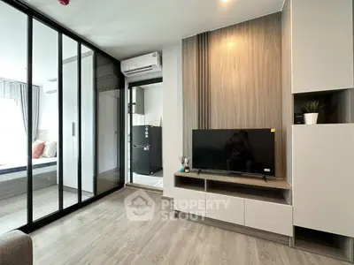 Modern living room with sleek design and glass partition leading to bedroom, featuring stylish furniture and decor.