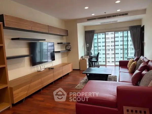 Spacious modern living room with red leather sofa and large TV, featuring city view.