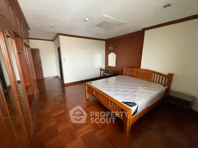 Spacious bedroom with wooden flooring and furniture, featuring a large bed and built-in wardrobe.