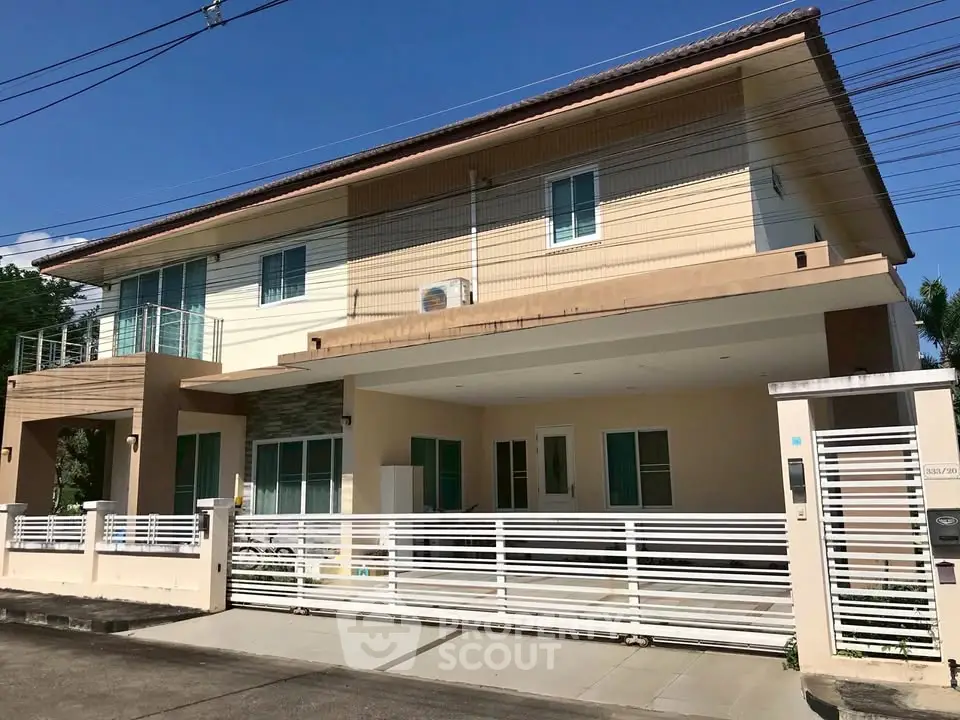 Modern two-story house with spacious balcony and gated entrance in a suburban neighborhood.