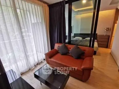 Modern living room with cozy sofa and glass partition leading to bedroom