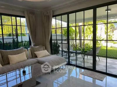 Spacious living room with large windows overlooking a lush garden, featuring modern furniture and elegant decor.