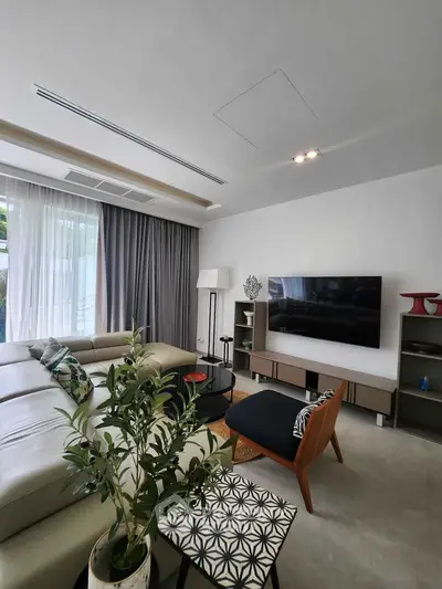 Modern living room with stylish furniture and large TV, featuring natural light and elegant decor.