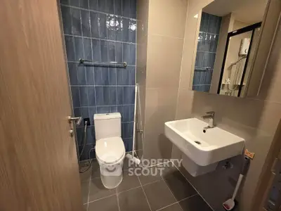 Modern bathroom with sleek design, featuring blue tiled wall, white fixtures, and a large mirror.