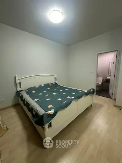 Cozy bedroom with floral bedspread and en-suite bathroom in modern apartment.