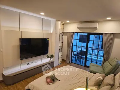 Modern living room with large TV, cozy seating, and balcony access in stylish apartment.