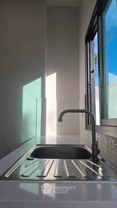 Modern kitchen sink with sleek faucet and natural light through window.