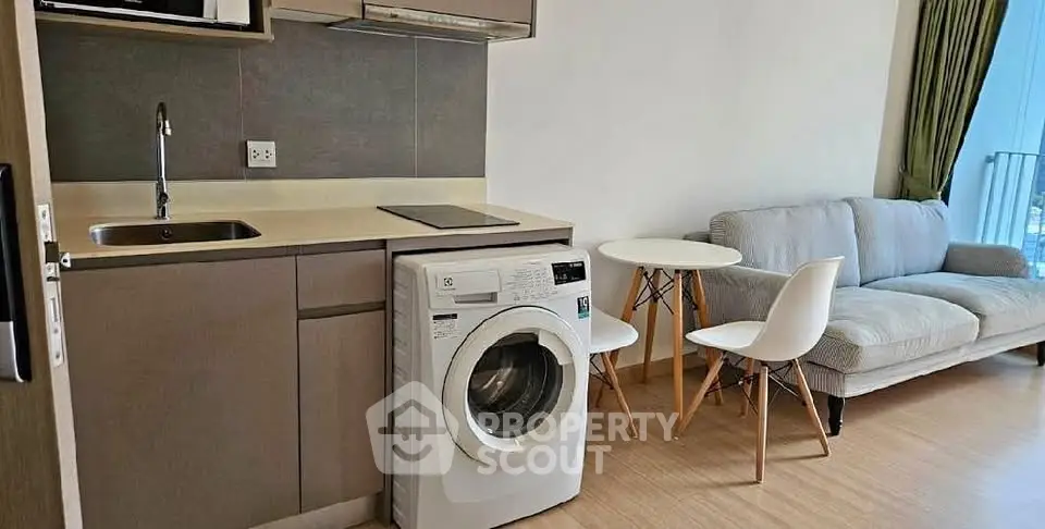 Modern compact living room with integrated kitchen and washing machine, featuring cozy sofa and dining area.