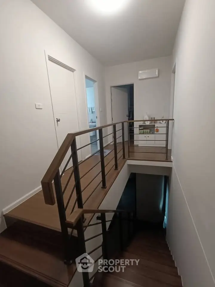Modern interior hallway with wooden stairs and railing, showcasing sleek design.