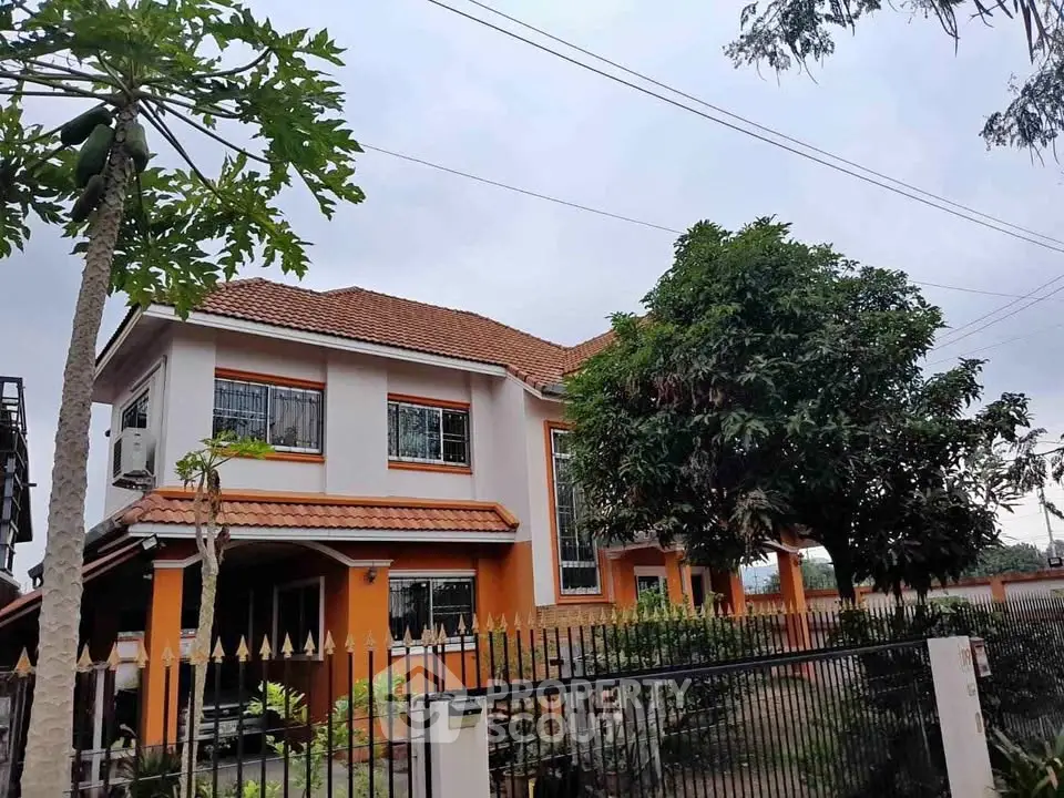 Charming two-story house with orange accents and lush garden in a serene neighborhood.