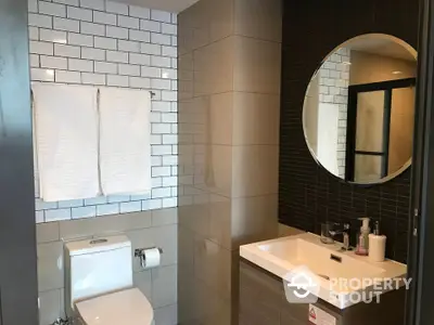 Modern bathroom with sleek tiles, round mirror, and contemporary fixtures, offering a stylish and functional space.