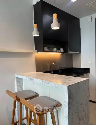 Modern kitchen with marble countertop and stylish pendant lights in a sleek apartment.