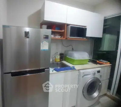 Modern kitchen with stainless steel fridge, washing machine, and microwave in compact layout.
