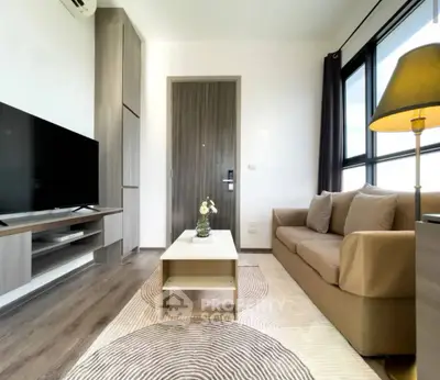Modern living room with stylish furniture and large TV, featuring natural light and elegant decor.