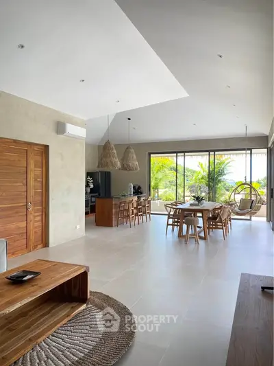 Spacious open-plan living room with modern decor and large windows overlooking lush greenery.