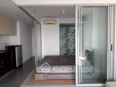 Modern studio apartment with glass sliding doors and compact kitchen area.