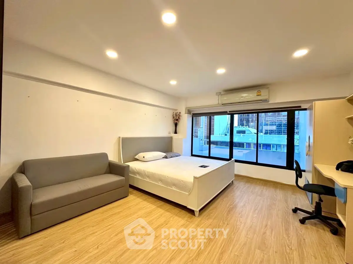 Spacious bedroom with modern furnishings and large window offering city views.