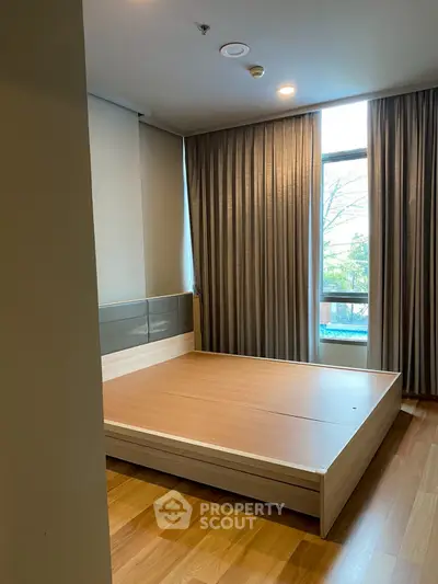 Spacious bedroom with large window and wooden flooring in modern apartment