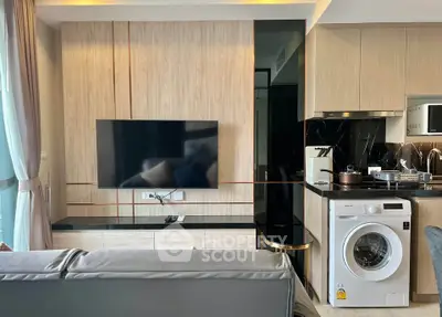 Modern living room with sleek TV setup and integrated kitchen featuring washing machine.