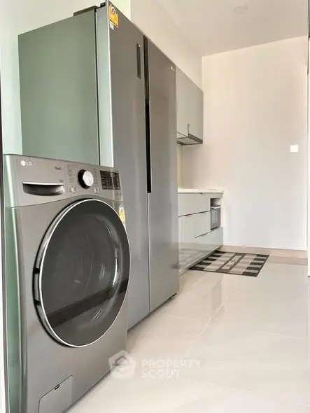 Modern kitchen with sleek appliances and glossy flooring, featuring a washing machine and refrigerator.
