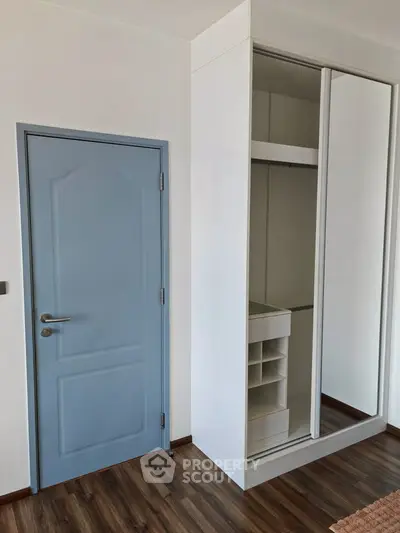 Modern bedroom with sleek built-in wardrobe and stylish blue door, featuring elegant wood flooring.