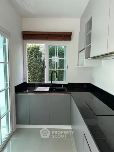 Modern kitchen with sleek black countertops and large window for natural light.