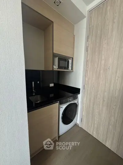 Compact kitchen with modern appliances including a washing machine and microwave, featuring sleek cabinetry.