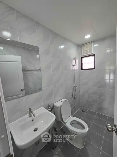 Modern bathroom with sleek fixtures and tiled walls, featuring a toilet, sink, and shower area.