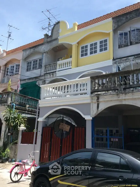 Charming townhouse with vibrant yellow facade and spacious balcony in a residential neighborhood.