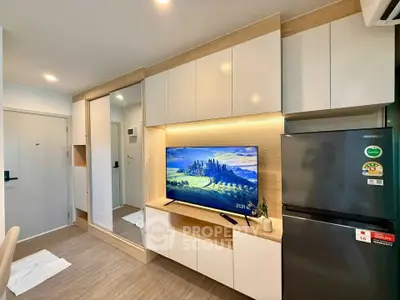 Modern living room with sleek cabinetry and large TV, featuring a stylish refrigerator and wood flooring.