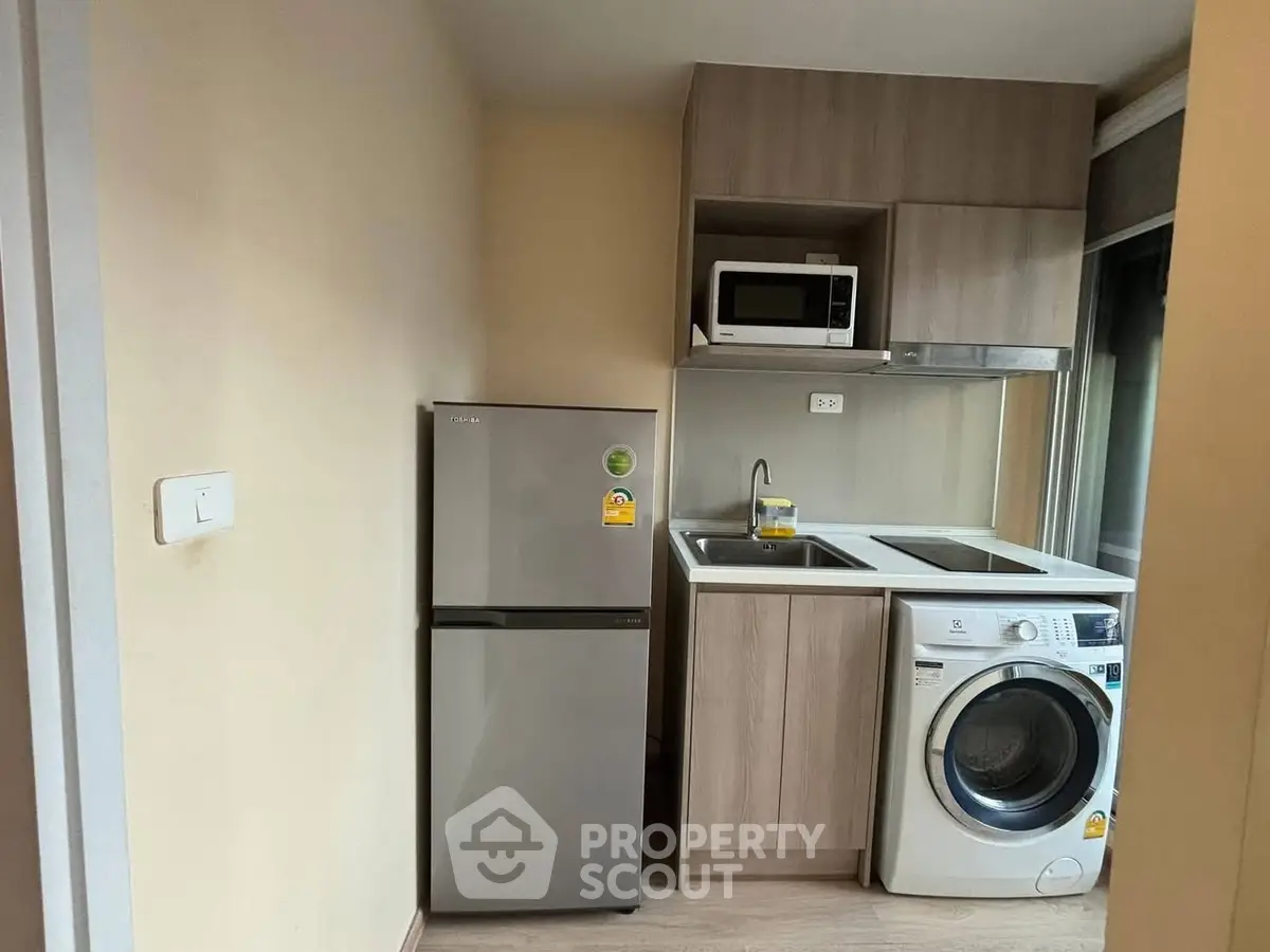 Compact kitchen with fridge, washing machine, and microwave in modern apartment.