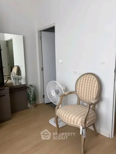 Cozy bedroom corner with elegant chair and fan, perfect for relaxation.