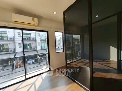 Modern apartment with large windows and balcony view, featuring sleek glass doors and wooden flooring.