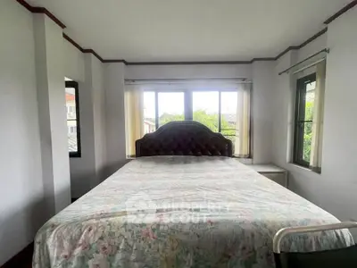 Cozy bedroom with large windows and floral bedspread, offering a serene and inviting atmosphere.