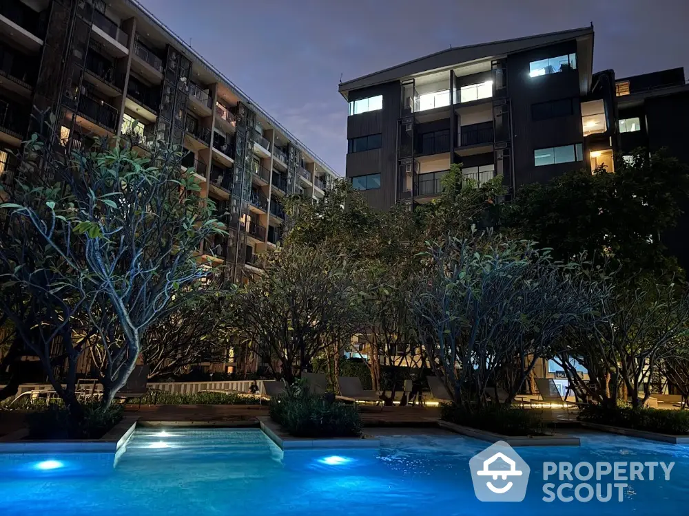 Stunning evening view of modern apartment complex with illuminated pool and lush landscaping.