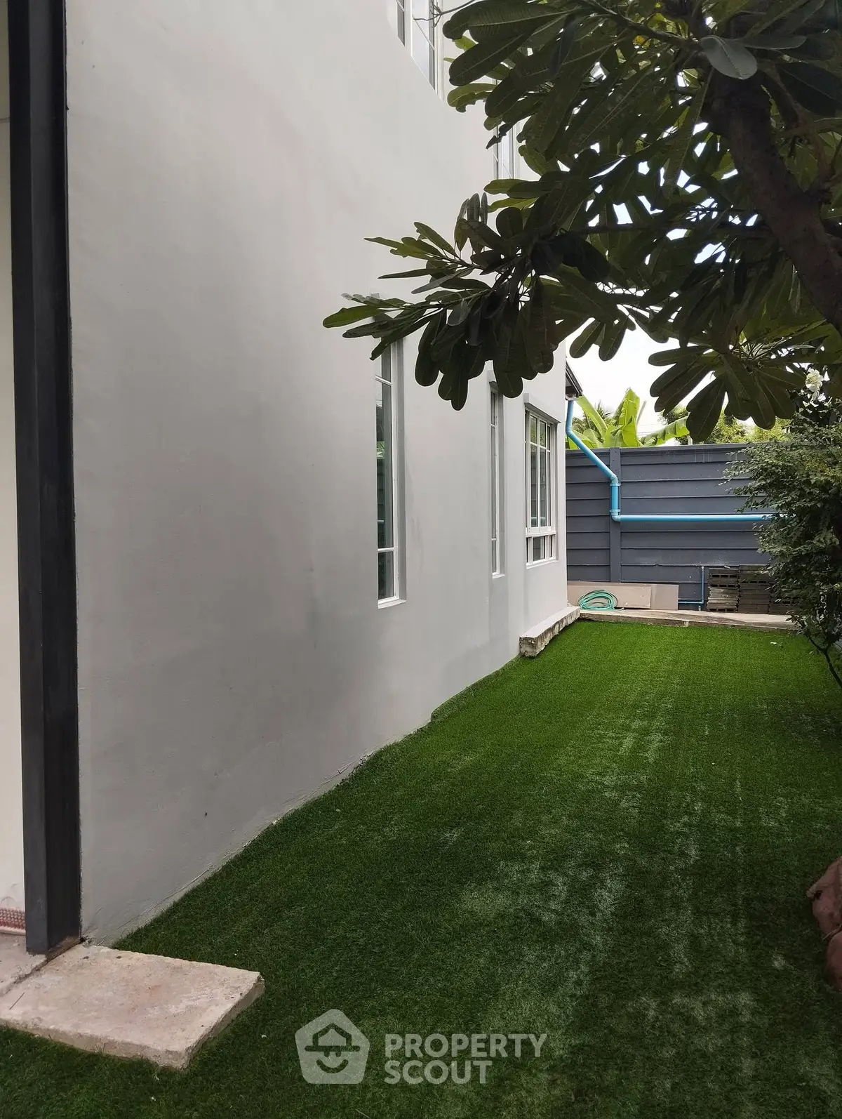 Charming side garden with lush artificial grass and modern building exterior, perfect for relaxation and outdoor activities.