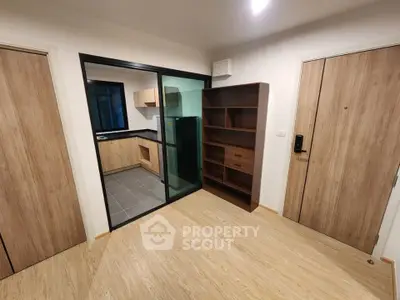 Modern apartment interior with open kitchen and wooden flooring, featuring sleek cabinetry and a glass partition.