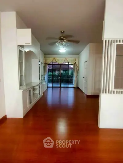 Spacious living room with wooden flooring and large windows opening to a balcony.