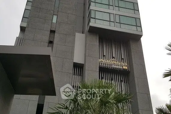 Modern high-rise building with sleek design and lush greenery at the entrance.