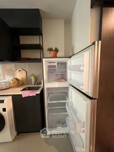 Modern kitchen with open fridge and washing machine, sleek cabinetry, and stylish decor.