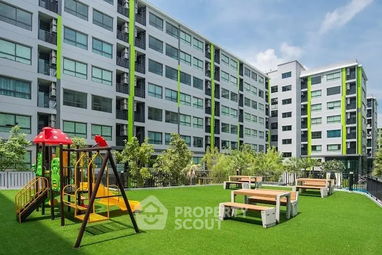 Modern apartment complex with playground and seating area on lush green lawn.