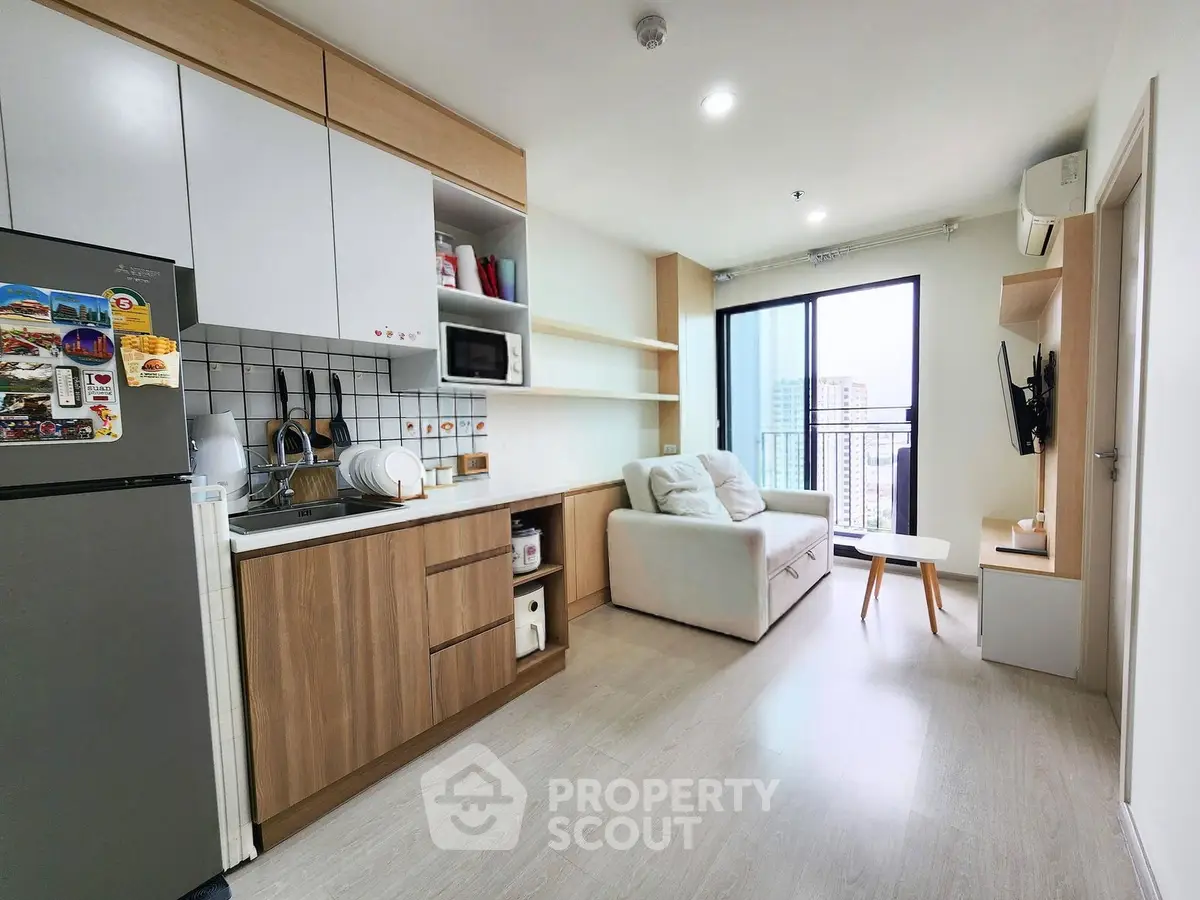 Modern open-layout living room with kitchen, featuring sleek cabinetry and a cozy sofa, ideal for urban living.