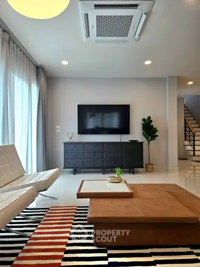 Modern living room with stylish furniture and large TV, featuring a chic rug and elegant decor.