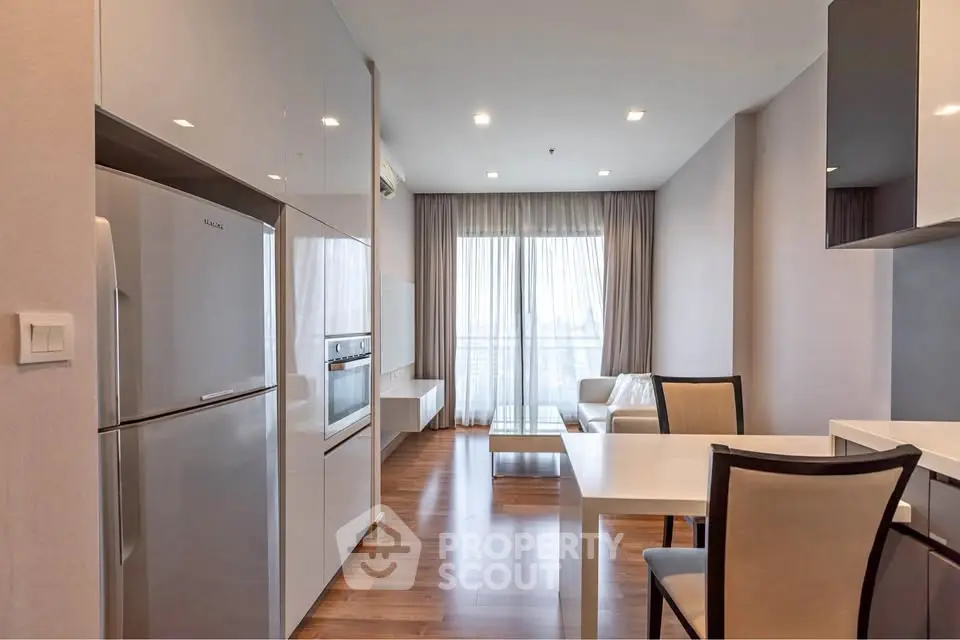 Modern apartment interior with sleek kitchen and cozy living area, featuring wooden flooring and natural light.