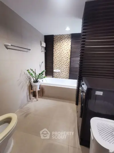 Modern bathroom with stylish bathtub and washing machine, featuring elegant tile design and indoor plant.