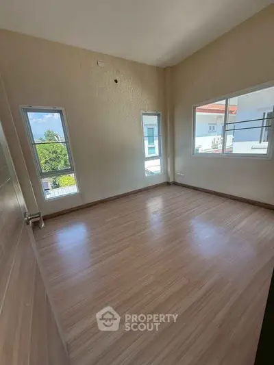 Spacious empty room with large windows and wooden flooring, perfect for customization.